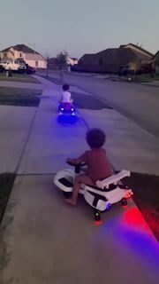 Two kids riding wiggle cars at dusk with lights on